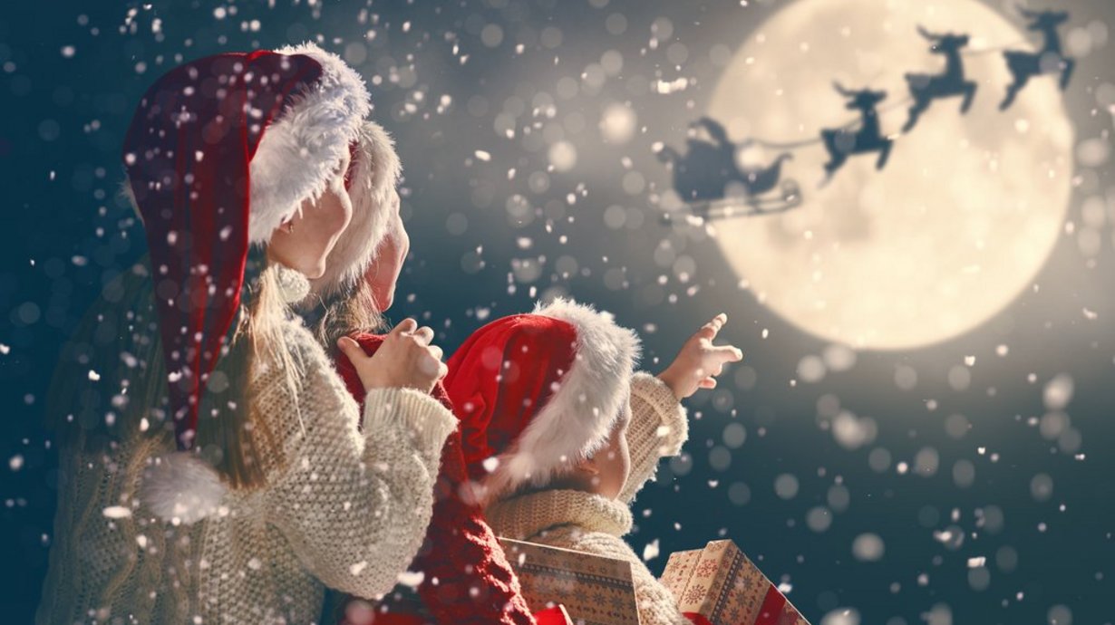 Kinder mit Weihnachtsgeschenken. Santa Claus fliegt mit seinem Schlitten vor dem Mond. 